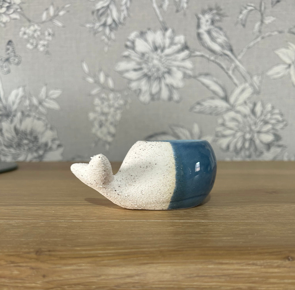 Ceramic whale figurine on a wooden surface with floral wallpaper in the background