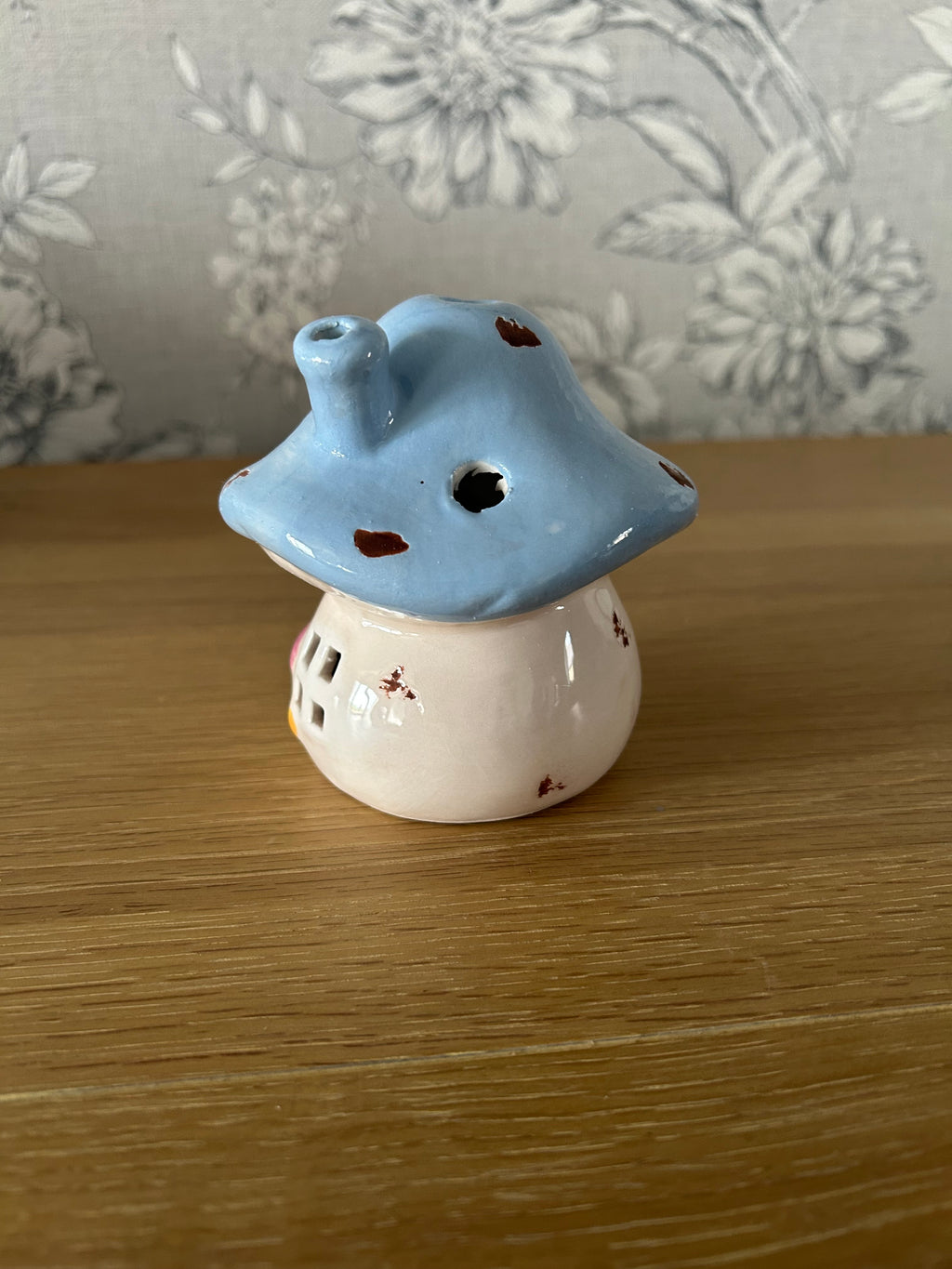 Ceramic mushroom shaped object on a wooden surface with floral-patterned fabric in the background.