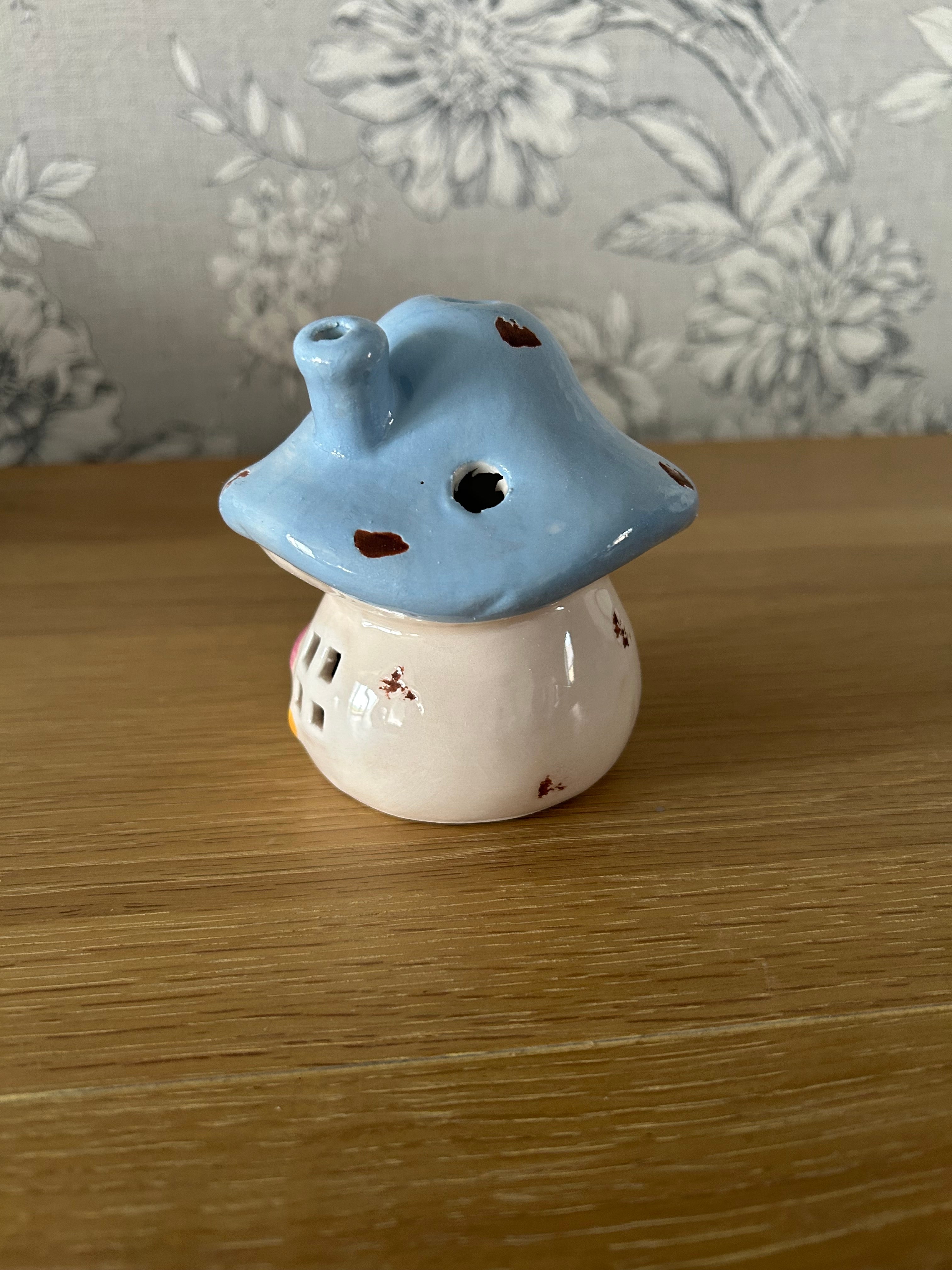 Ceramic mushroom shaped object on a wooden surface with floral-patterned fabric in the background.