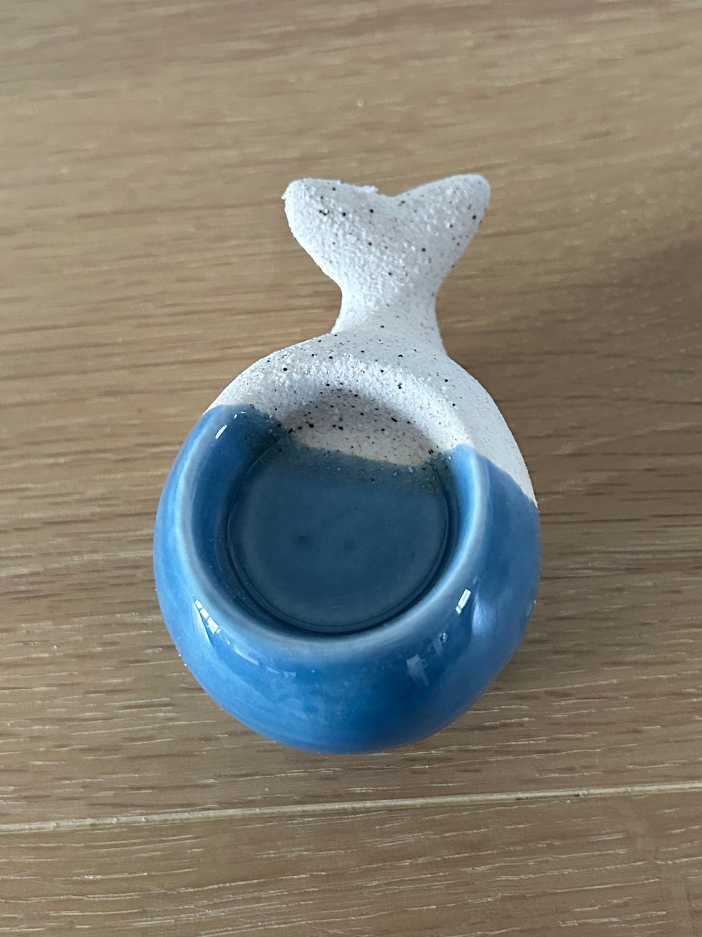 Ceramic whale-shaped container with a blue interior on a wooden surface