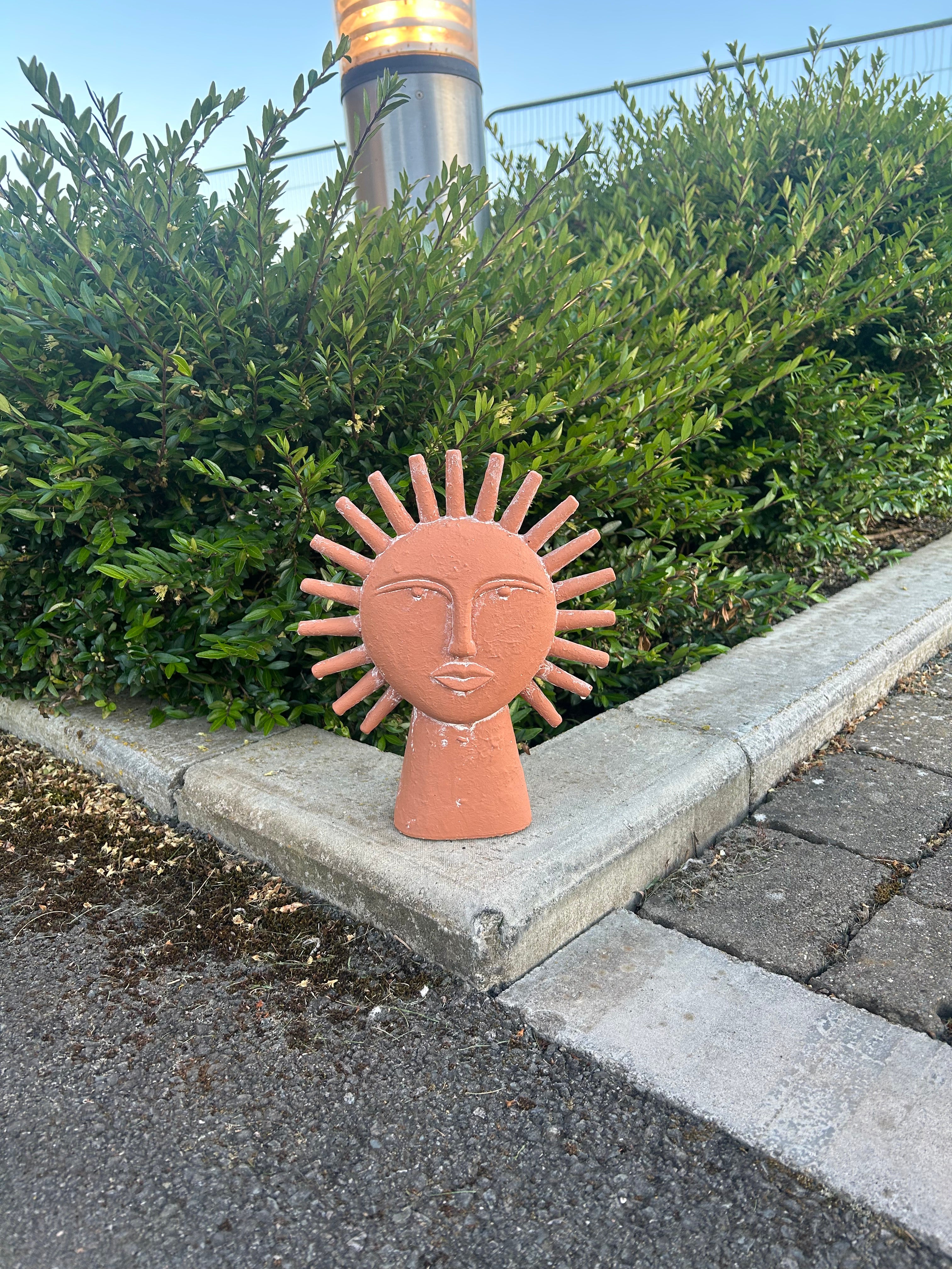 Decorative sun-shaped object on a sidewalk next to a bush