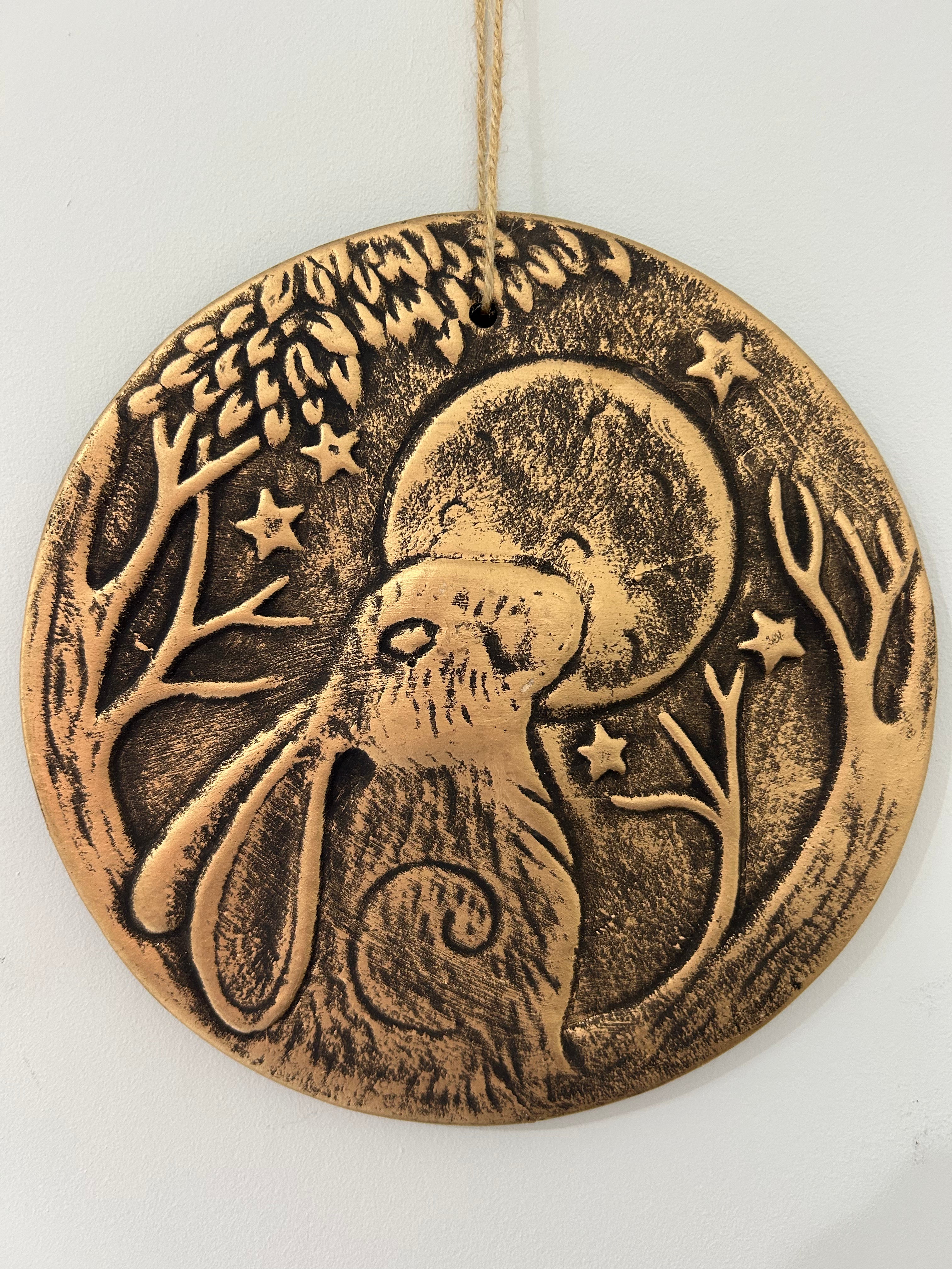 Bronze-colored decorative plaque with a rabbit and moon design on a white background